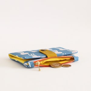 May include: A small blue zippered wallet with a yellow flap and a white pattern of rabbits. The wallet is open and has a few coins inside.