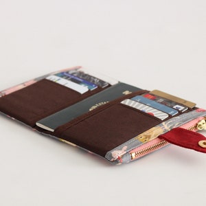 May include: A gray and pink floral patterned wallet with a red zipper pull and a brown interior. The wallet is open and has several cards and a passport inside.