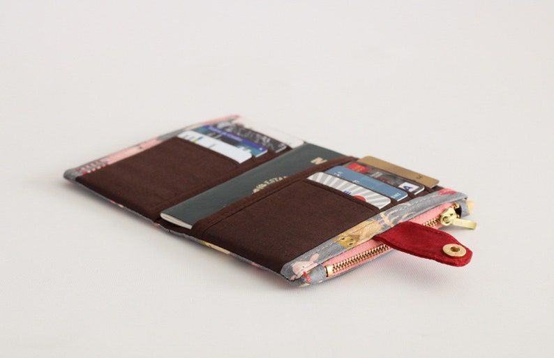 May include: A gray and pink floral patterned wallet with a red zipper pull and a brown interior. The wallet is open and has several cards and a passport inside.