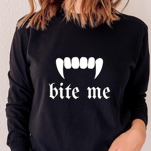 May include: Black long-sleeved sweatshirt with a white graphic of vampire fangs and the text "bite me" in a gothic font.