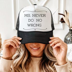 May include: A black and white trucker hat with the text "MS. NEVER DO NO WRONG" in black. The hat has a white front panel and a black brim and mesh back. The text is centered on the front panel.
