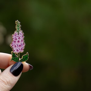 May include: A pink and green enamel pin of a foxglove flower.