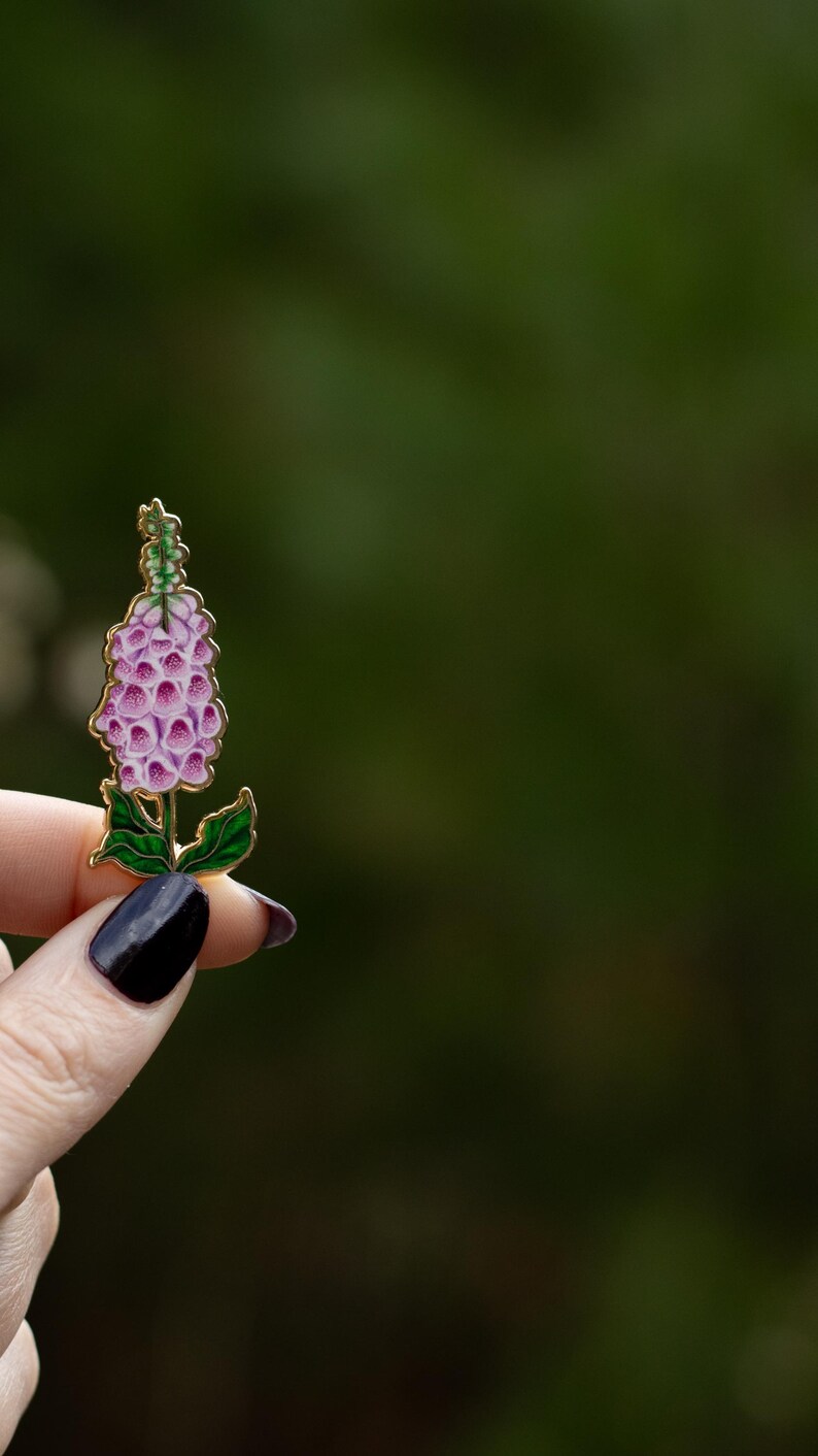 May include: A pink and green enamel pin of a foxglove flower.
