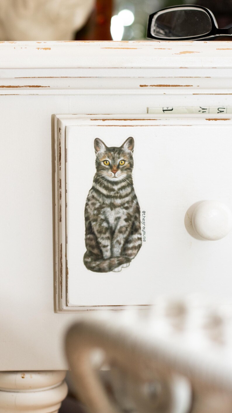 May include: A white drawer with a gray and white tabby cat illustration. The drawer has a white knob and the text "@thegraymuse" is printed on the right side of the image.