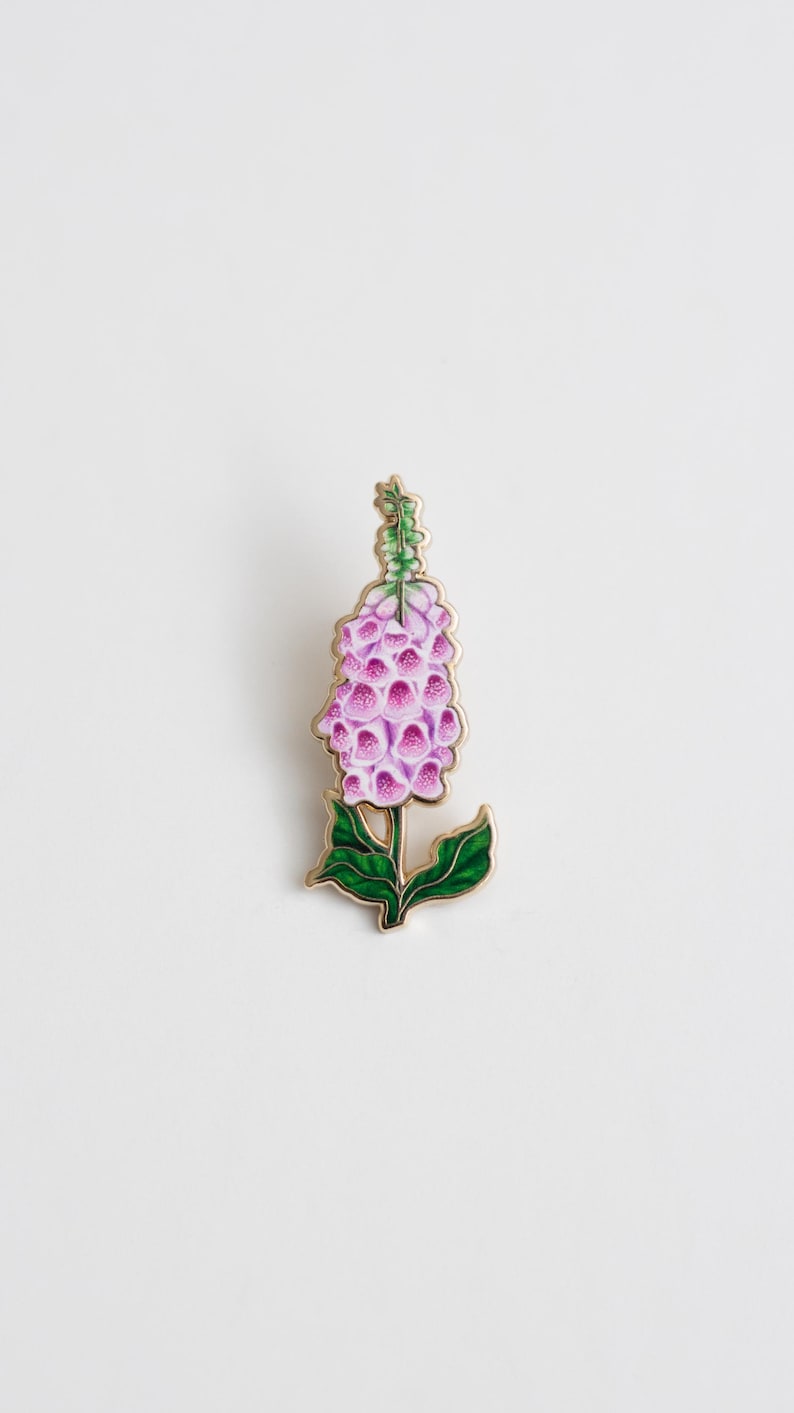 May include: A gold-tone enamel pin featuring a pink and green foxglove flower.