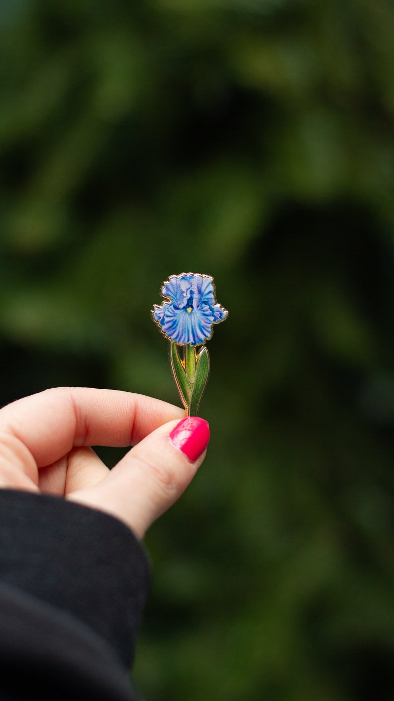 May include: A blue and green enamel pin featuring a detailed iris flower.