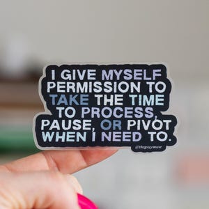 May include: A sticker with the text "I GIVE MYSELF PERMISSION TO TAKE THE TIME TO PROCESS, PAUSE, OR PIVOT WHEN I NEED TO." in white and blue lettering on a black background. The sticker is held by a hand with bright pink nail polish.