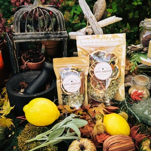 May include: Two clear plastic bags filled with dried herbs, flowers, and citrus fruit slices. The bags are labeled "Anti-Anxiety". The bags are surrounded by fall foliage, lemons, and other decorative items.