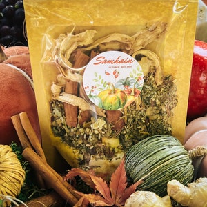 May include: A clear cellophane bag filled with dried herbs and spices, including cinnamon sticks. A round sticker with the word "Samhain" and pumpkins is affixed to the bag. The background includes pumpkins, apples, and fall foliage.
