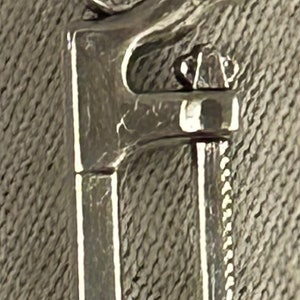 May include: A silver charm necklace with a detailed, stylized design of a wrench. The charm is attached to a silver chain.