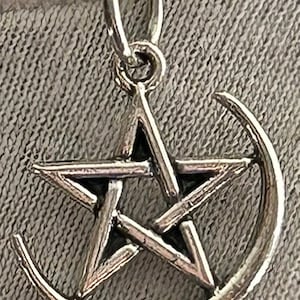 May include: A silver pendant featuring a pentagram with a crescent moon design. The pendant is on a silver chain.