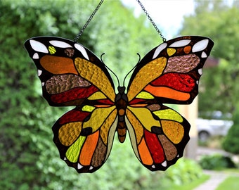 May include: A stained glass butterfly suncatcher with a yellow, orange, red, and brown color scheme. The butterfly is hanging from a chain.