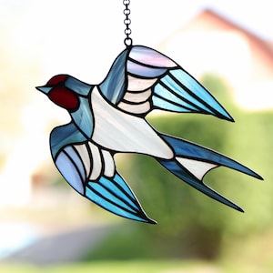 May include: A stained glass swallow with blue, white, and red accents. The swallow is in flight with its wings spread out.