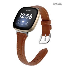 May include: Brown leather watch band with a silver buckle. The band is compatible with a smartwatch with a square face. The watch face displays the time, date, and heart rate.