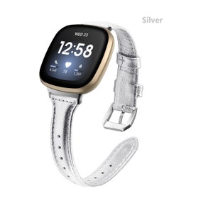 May include: A silver leather watch band with a gold-colored smartwatch face displaying the time 12:58 and the date WED 23. The watch face also shows heart rate, steps, and calories burned.