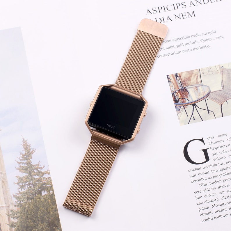 K&ouml;nnte beinhalten: Eine ros&eacute;goldene Armbanduhr mit einem quadratischen Zifferblatt und dem Wort "fitbit" auf dem Zifferblatt.