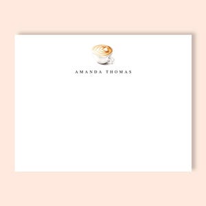 May include: White stationery with a watercolor illustration of a latte with foam art. The text "AMANDA THOMAS" is printed in a thin, black font below the coffee cup. The background is a light peach color.