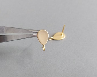 May include: A pair of gold-toned earring findings with a teardrop shape and a small loop at the bottom. The findings are being held by a pair of pliers.