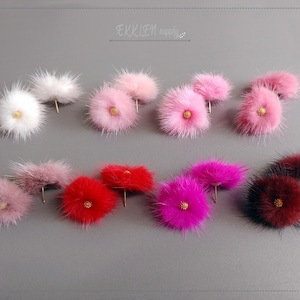 May include: A set of 10 pairs of fluffy faux fur earrings in various colors, including pink, white, red, and burgundy. Each earring features a small gold-colored center.