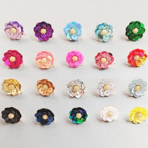 May include: Assortment of 20 colorful flower-shaped sequins with gold accents. The sequins are arranged in rows on a light gray surface.