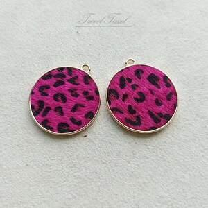 May include: Two gold-rimmed round pendants with a pink and black leopard print design.