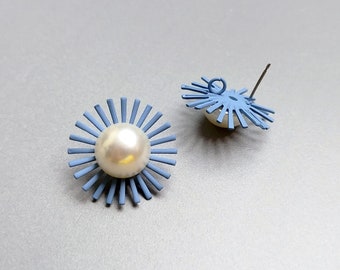 May include: A pair of blue metal earrings with a white pearl in the center of each earring. The earrings are shaped like a sunburst with multiple points.