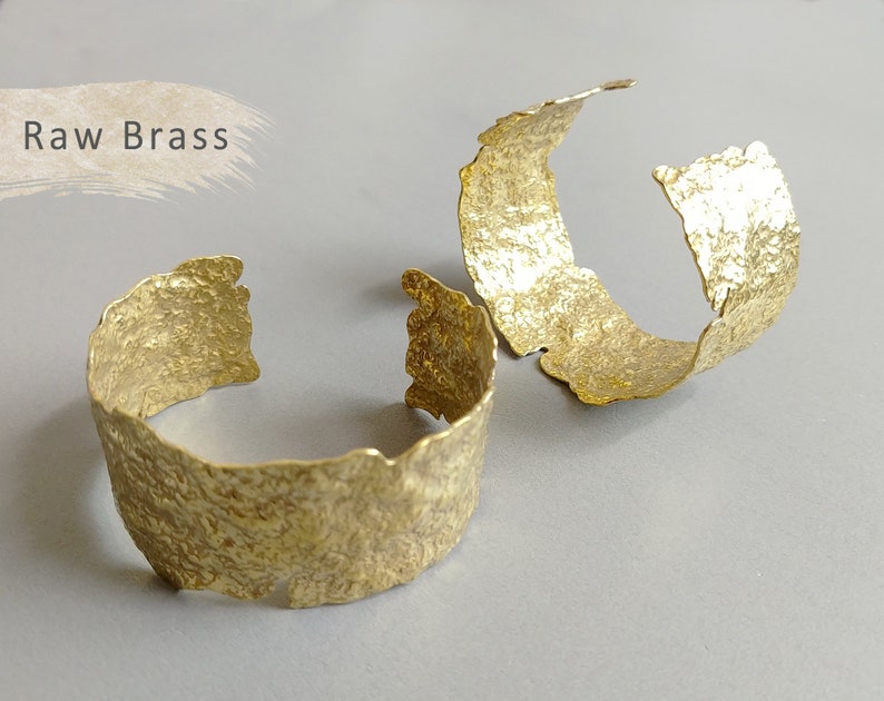 May include: Two raw brass bracelets with a hammered texture. The bracelets are open and have a rough, organic shape.