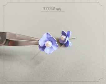 May include: A pair of lavender flower earrings with a pearl center. The earrings are on a gray surface.