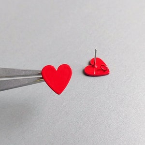 May include: A pair of red heart-shaped stud earrings. The earrings are made of metal and have a post backing.