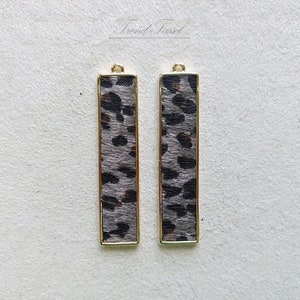 Puede incluir: Dos colgantes de barra de metal dorado con un diseño de estampado de leopardo gris y negro.