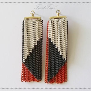 May include: A pair of long, geometric earrings with a silver, black, and orange chain design. The earrings have a gold hook closure.