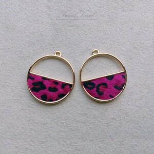 May include: A pair of gold-toned earrings with a pink and black leopard print design. The earrings are circular and have a half-circle of the print on the bottom half of the earring.