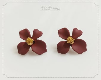 May include: A pair of maroon flower-shaped earrings with gold centers. The earrings are made of a smooth, matte material.