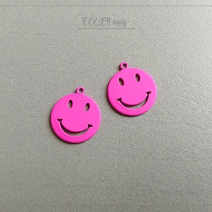 May include: Two pink metal smiley face charms with a cutout design.