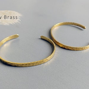 May include: Two gold-toned hammered metal bracelets. The bracelets are simple and minimalist in design.