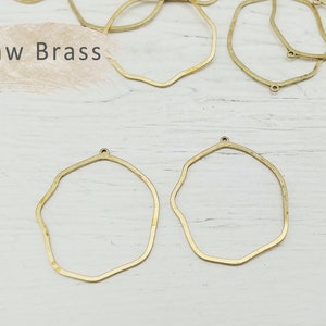 May include: Raw brass irregular shaped hoops with a small hole at the top. The hoops are on a white wooden surface.