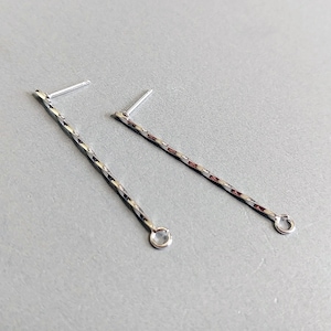 Può includere: Un paio di orecchini d'argento con un design intrecciato e un piccolo cerchio alla fine di ogni orecchino.