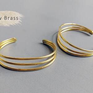May include: Two gold-toned, raw brass bangles. Each bangle is made of three thin, overlapping bands.