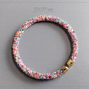 May include: A colorful, sparkly bangle bracelet with a gold clasp. The bracelet is made of small, iridescent beads that create a shimmering effect.