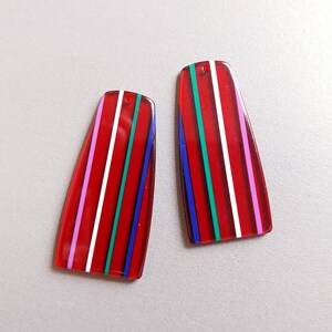 May include: Two red, white, blue, and pink striped acrylic earrings. The earrings are rectangular in shape and have a glossy finish.