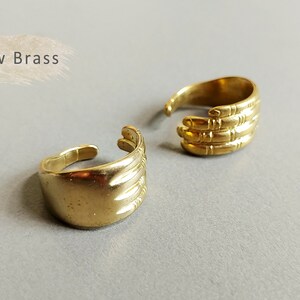 May include: Two gold-toned rings with a hand design. The rings are made of raw brass and have a textured finish.