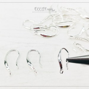 May include: Silver earring hooks, a close-up of three hooks with a pair of pliers in the background.  The hooks are a simple, elegant design.