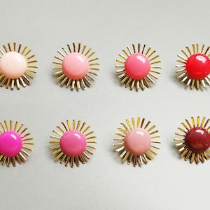 May include: Set of eight gold sunburst earrings with pink, red, and burgundy colored glass centers.