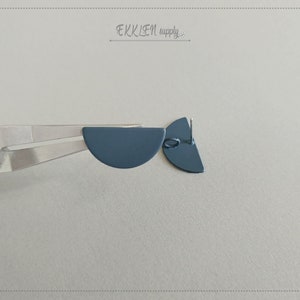 May include: A pair of dark blue half-circle earrings with silver posts being held by pliers.