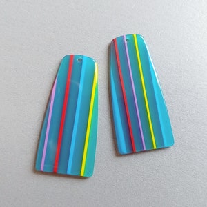May include: Two turquoise blue, striped, plastic earring blanks with a hole at the top. The stripes are red, yellow, light blue, purple, and green.