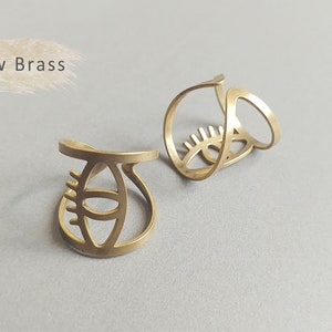 May include: Two gold-toned metal rings with an eye design. The rings are made of raw brass and have a simple, minimalist style.