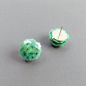 Puede incluir: Un par de pendientes de lentejuelas verdes con postes dorados. Los pendientes son redondos y tienen un efecto 3D.