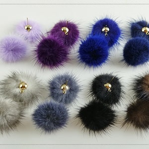 May include: Assortment of 10 faux fur pom poms in various colors, including gray, brown, purple, blue, and black. Each pom pom has a gold metal loop for attaching to a project.