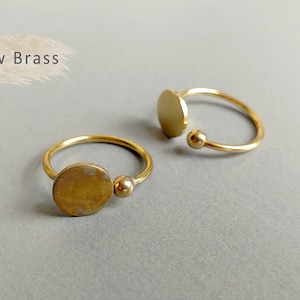 May include: Two gold rings with a round disc design. The rings are made of raw brass and have a simple, minimalist style.
