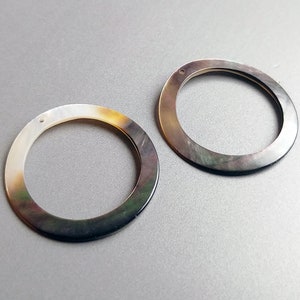 May include: Two round, black and white shell rings with a hole in the center. The rings are about 2 inches in diameter.